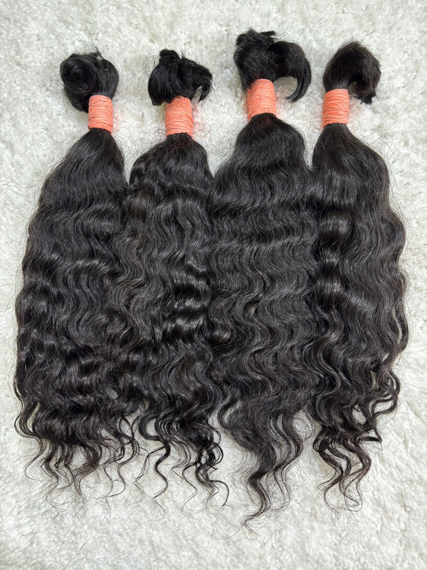 Multiple bundles of raw Indian curly bulk hair are displayed, tied at the ends with orange bands.
