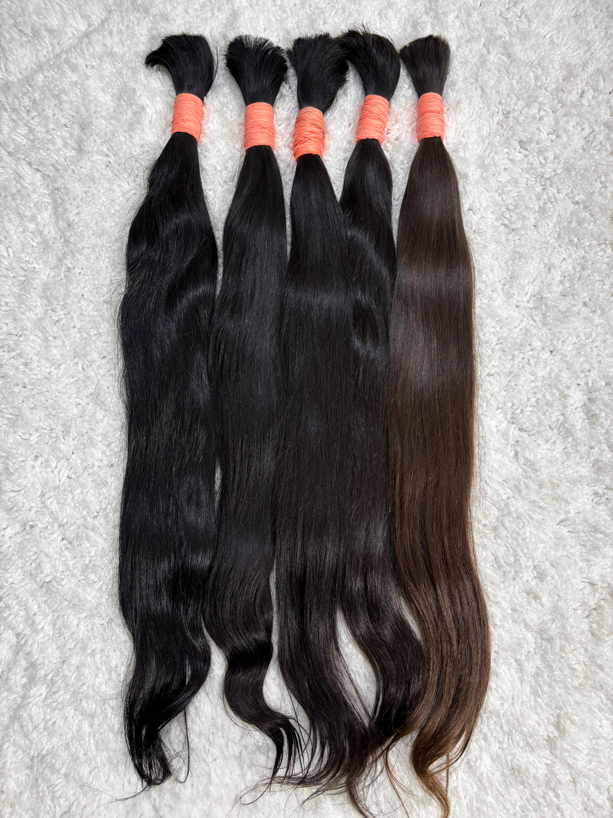 Multiple packs of raw Indian straight bulk hair extensions laid out on a surface.