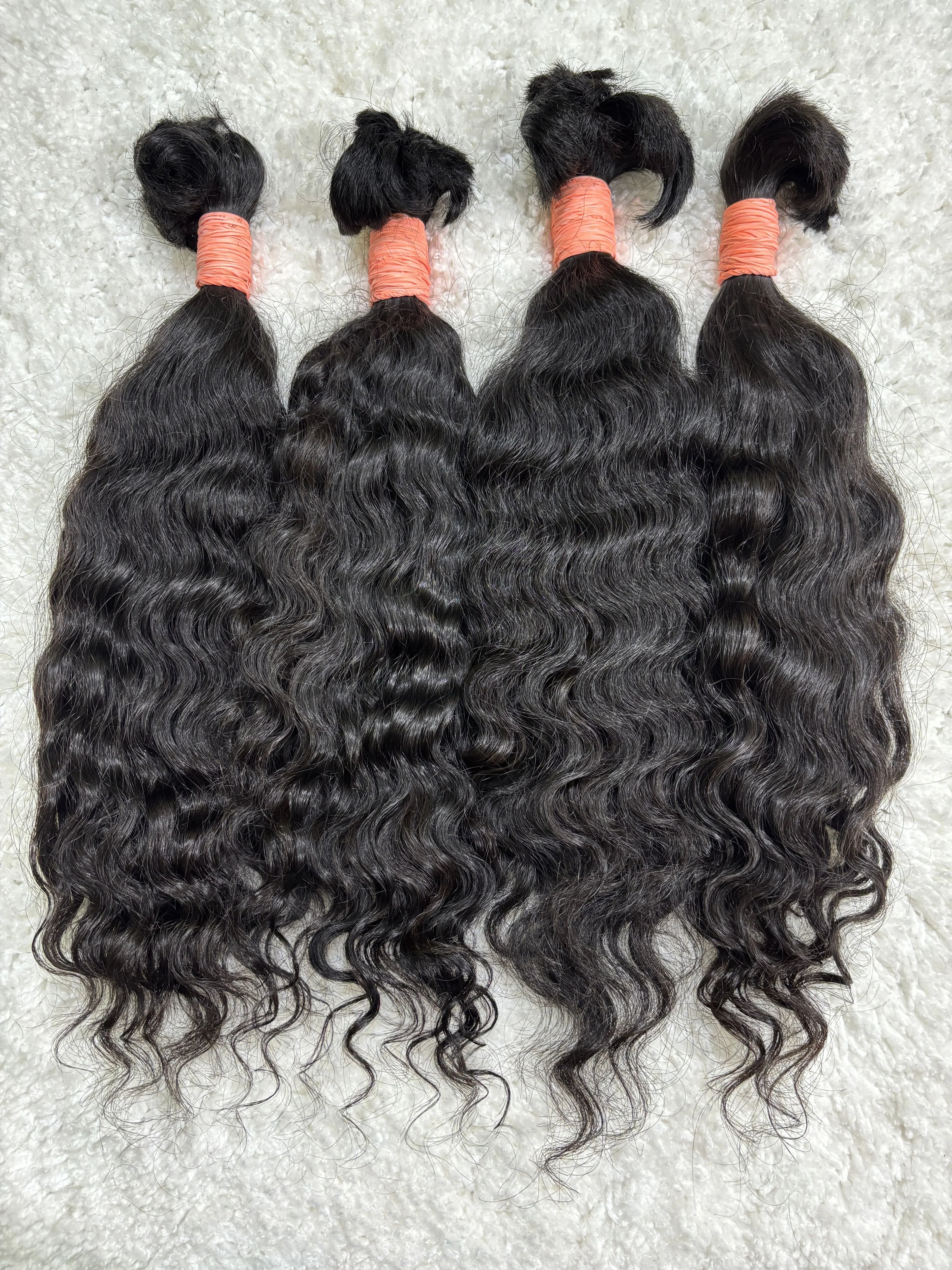 Multiple bundles of raw Indian curly bulk hair are displayed, tied at the ends with orange bands.