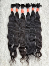 Multiple bundles of raw Indian wavy bulk hair are displayed, tied at the ends with red bands. The hair appears dark and wavy, with a natural texture.